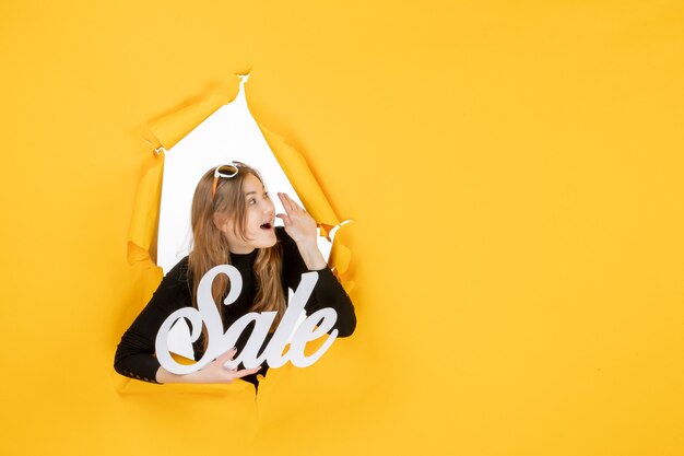 Front view young female holding sale writing through torn paper hole in the wall