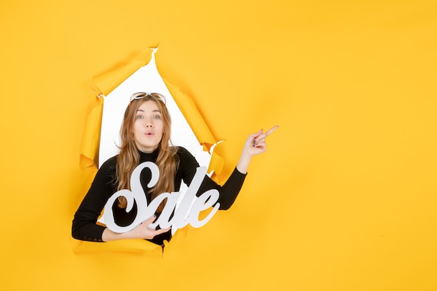 Free photo front view young female holding sale writing through torn paper hole in the wall