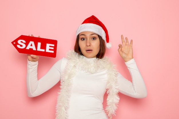 Free photo front view young female holding sale written figure on pink wall color holiday new year snow christmas