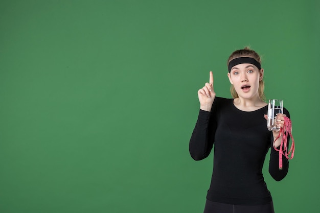 Front view young female holding waist measure and glass of water on green