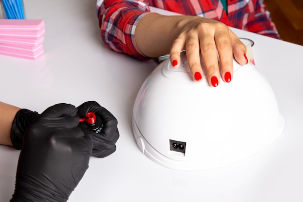 A front view young female manicure with black gloves doing manicure on white