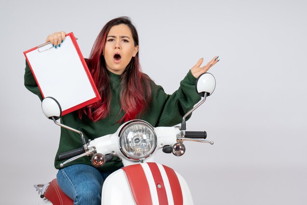 Front view young female on motorcycle holding note for signature on a white wall