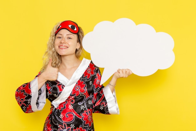 Front view young female in night robe eye mask holding huge white sign smiling on yellow wall sleep night bed model color