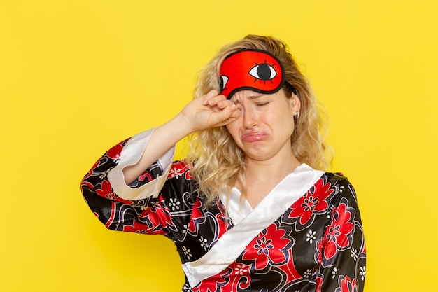 Free photo front view young female in night robe and wearing eye mask preparing to sleep fake crying on light yellow wall sleep female model night bed