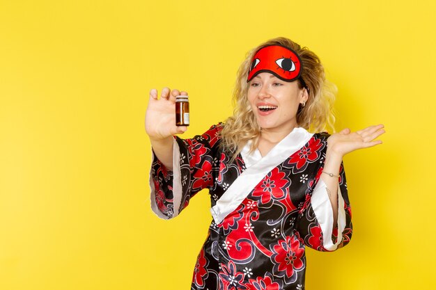 Front view young female in night robe and wearing eye mask preparing to sleep holding flask with pills on yellow wall sleep female darkness model night