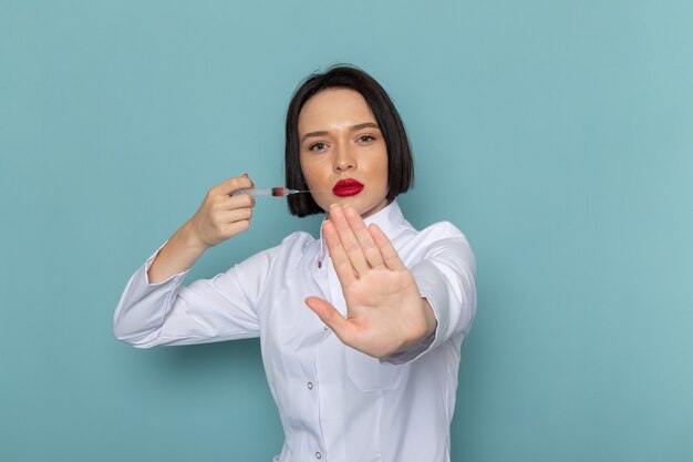 A front view young female nurse in white medical suit and blue stethoscope injecting herself on the blue desk medicine hospital doctor