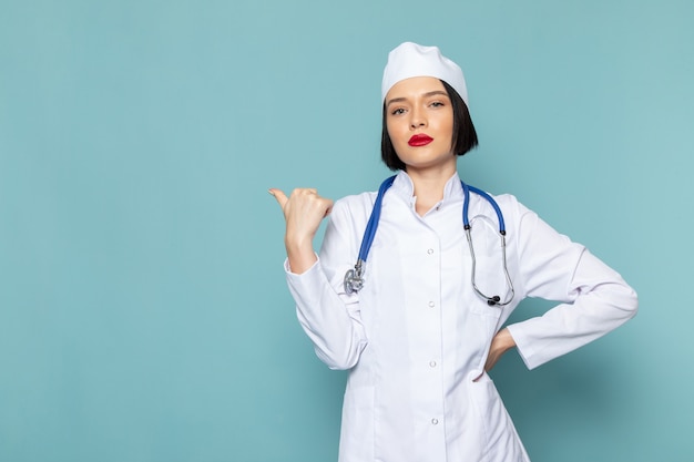 A front view young female nurse in white medical suit and blue stethoscope posing on the blue desk medicine hospital doctor color