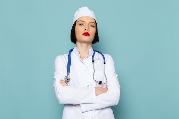 A front view young female nurse in white medical suit and blue stethoscope posing on the blue desk medicine hospital doctor