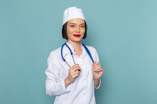 A front view young female nurse in white medical suit and blue stethoscope smiling on the blue desk medicine hospital doctor