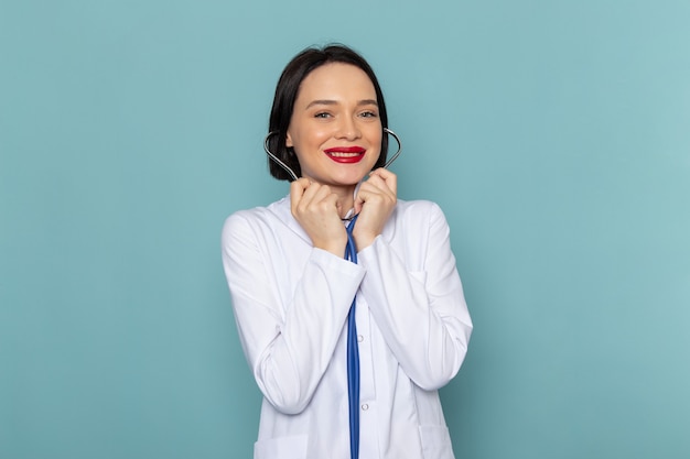 A front view young female nurse in white medical suit and blue stethoscope smiling on the blue desk medicine hospital doctor