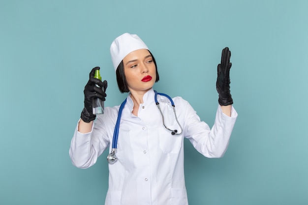 A front view young female nurse in white medical suit and blue stethoscope spraying her hands on the blue desk medicine hospital doctor