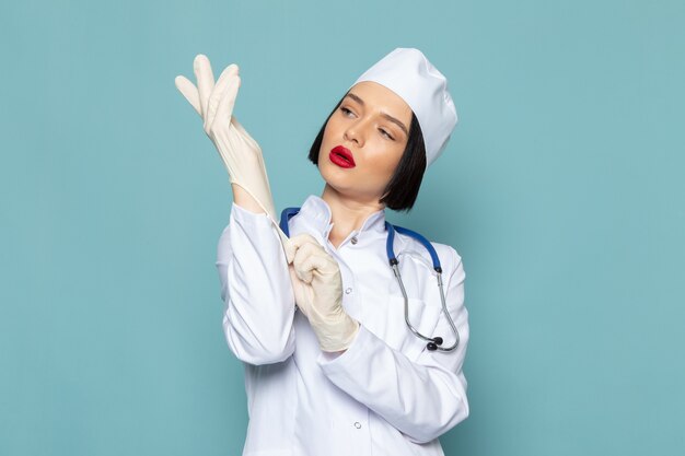 A front view young female nurse in white medical suit and blue stethoscope wearing white gloves on the blue desk medicine hospital doctor