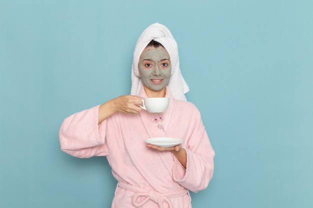 Free Photo front view young female in pink bathrobe after shower drinking coffee with smile on blue wall cleaning beauty clean water selfcare cream shower