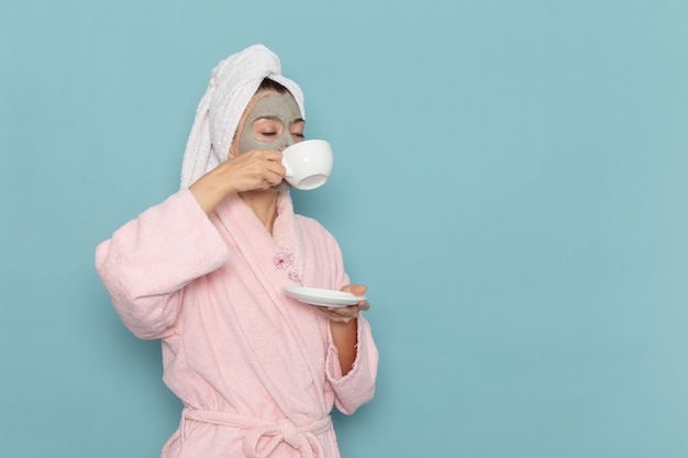 Front view young female in pink bathrobe drinking coffee on blue wall cleaning beauty clean water selfcare cream shower