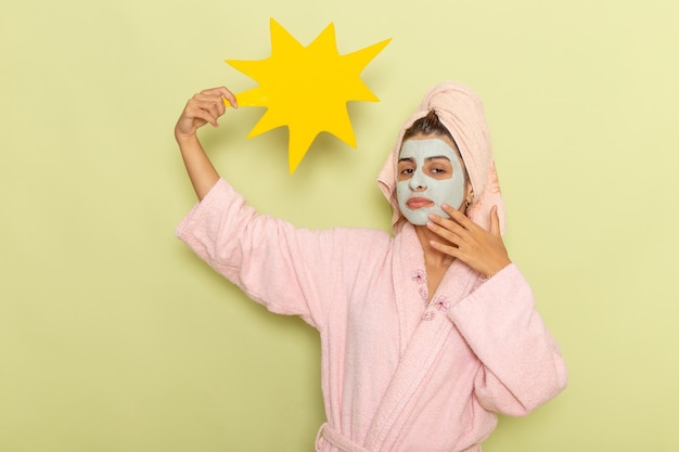 Free Photo front view young female in pink bathrobe holding big yellow sign on a green surface