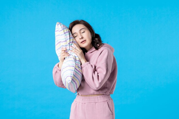 Front view young female in pink pajamas holding pillow on blue wall night color bed rest emotions model dream woman sleep