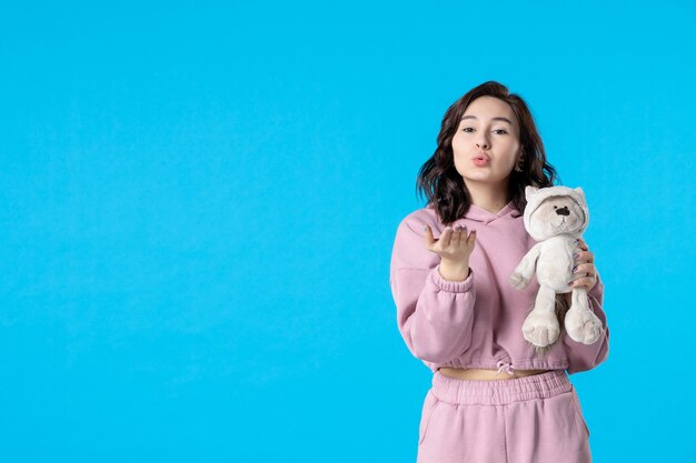 Front view young female in pink pajamas with little toy bear on blue