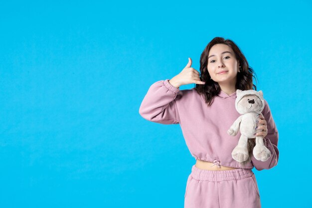 Front view young female in pink pajamas with little toy bear on blue