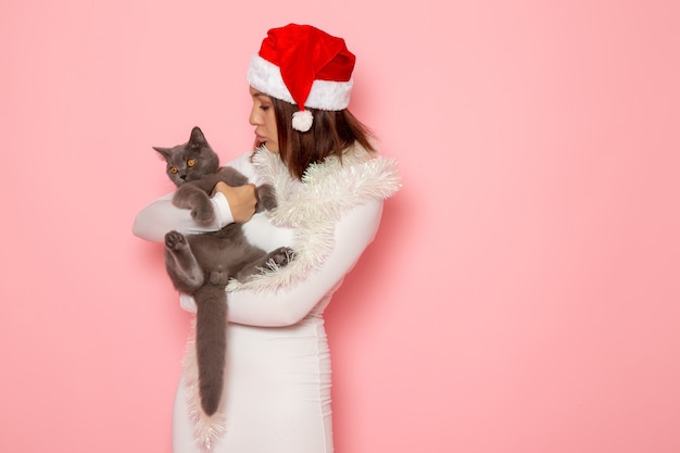 Free Photo front view of young female in red cap holding cute grey kitten on pink wall