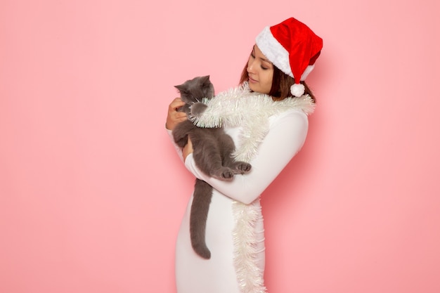 Free Photo front view of young female in red cap holding cute grey kitten on pink wall