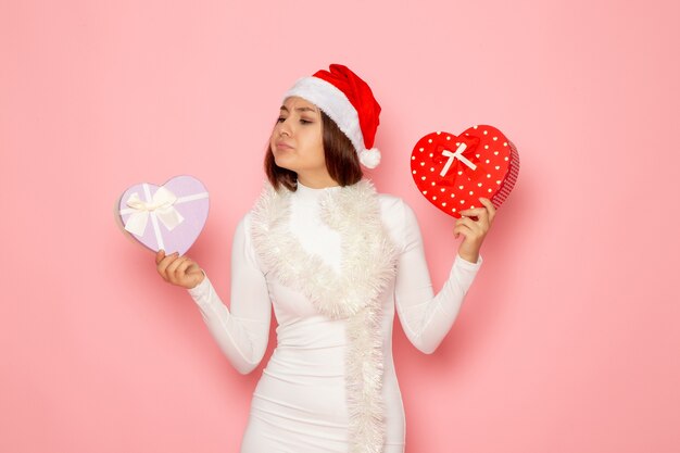 Front view of young female in red cap holding heart shaped presents on pink wall