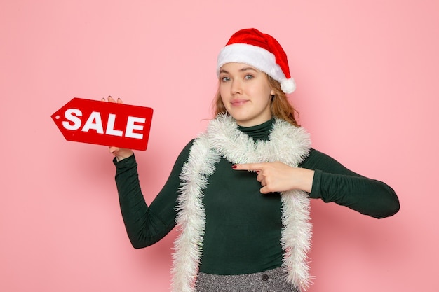 Front view of young female in red cap holding sale writing on pink wall