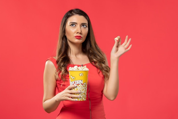 Free Photo front view young female in red shirt holding popcorn on the red surface