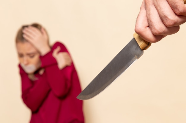 Front view young female in red shirt with tied mouth scared of knife on the cream space female cloth  photo