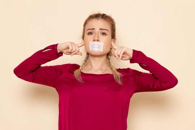 Front view young female in red shirt with tied mouth shutting her ears on the cream space female cloth  photo violence domestic