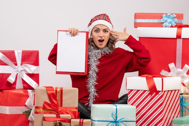 Front view young female sitting around christmas presents with note