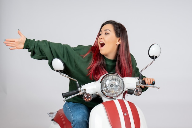 Front view young female sitting on motorcycle white wall