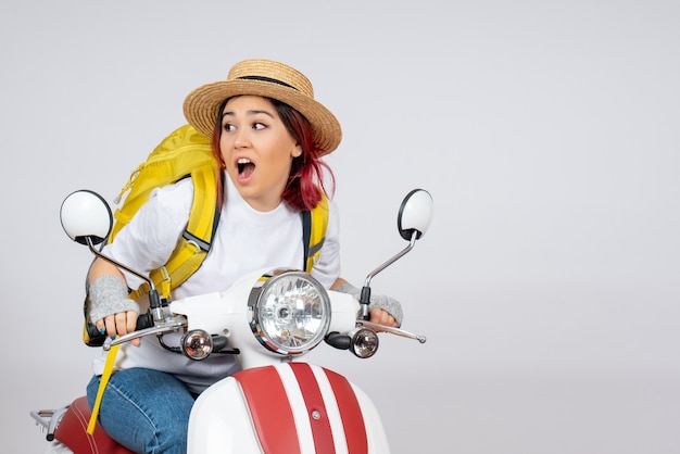 Front view young female sitting on motorcycle with backpack and hat white wall