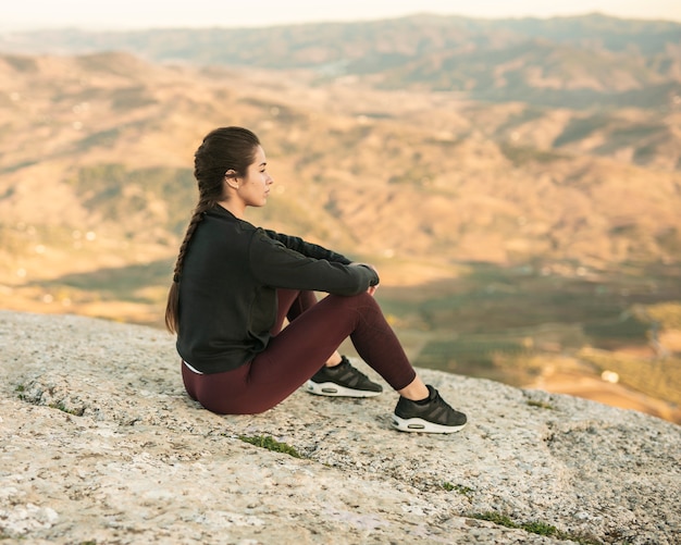 Free Photo front view young female sitting on top of mountain