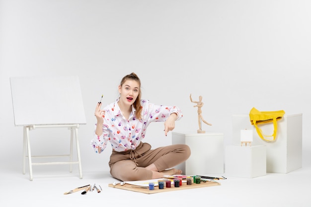 Free Photo front view young female sitting with paints and easel for drawing on white background