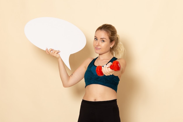 Free photo front view young female in sport outfit holding dumbbells and white speech bubble