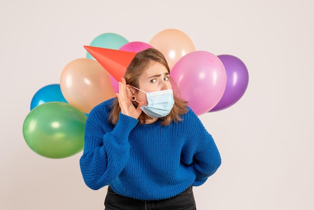 Front view young female in sterile mask hiding colorful balloons behind her back