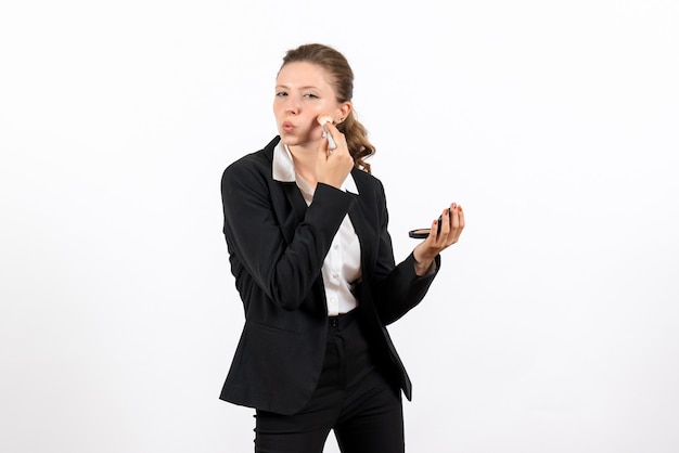 Front view young female in strict classic suit doing her make-up on white background woman job costume business serious