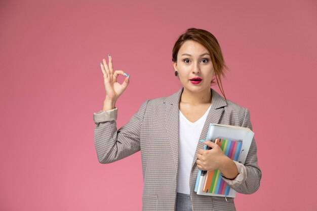 Front view young female student in grey coat with copybooks on pink background lessons university college study