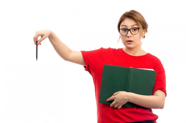 A front view young female student in red t-shirt holding green copybook on the white