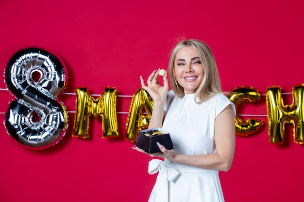 Free photo front view young female in white dress posing with delicious candies on decorated red womens day