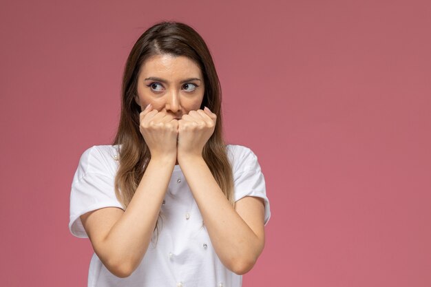 Front view young female in white shirt covering her mouth with scared expression 