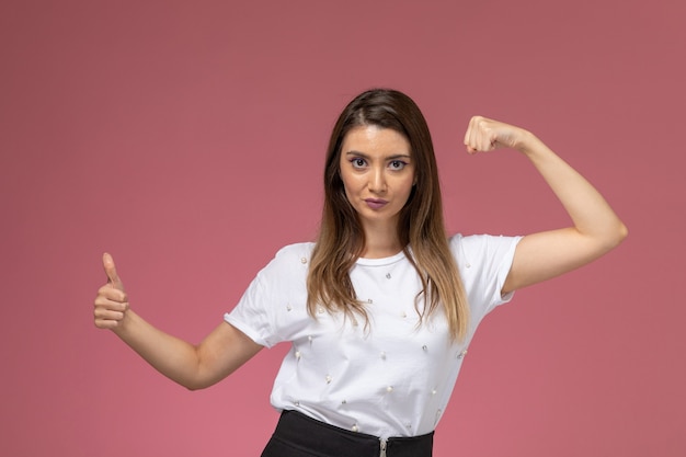 Front view young female in white shirt flexing and showing like sign, color woman model posing woman