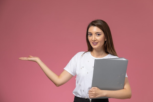 Front view young female in white shirt holding grey file on pink wall, model woman