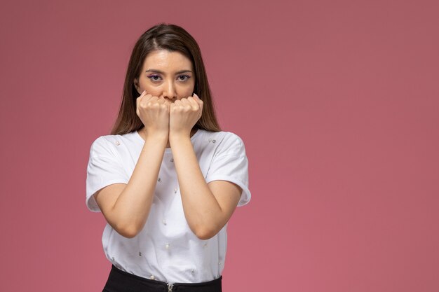 Front view young female in white shirt posing with squeezed fists on pink wall, color model woman pose