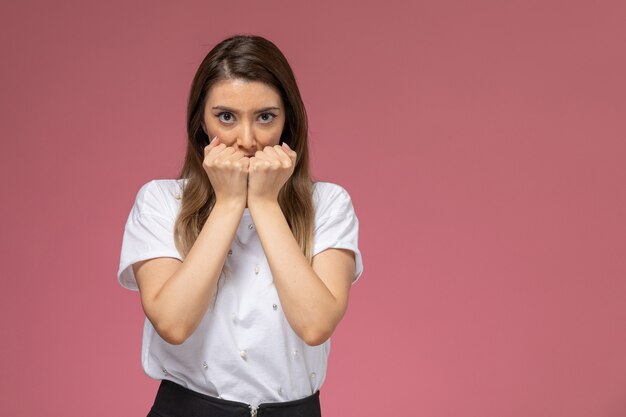 Front view young female in white shirt with squeezed fists on the pink wall, model woman