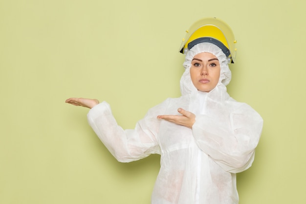 Front view young female in white special suit and yellow helmet posing on the green space job 