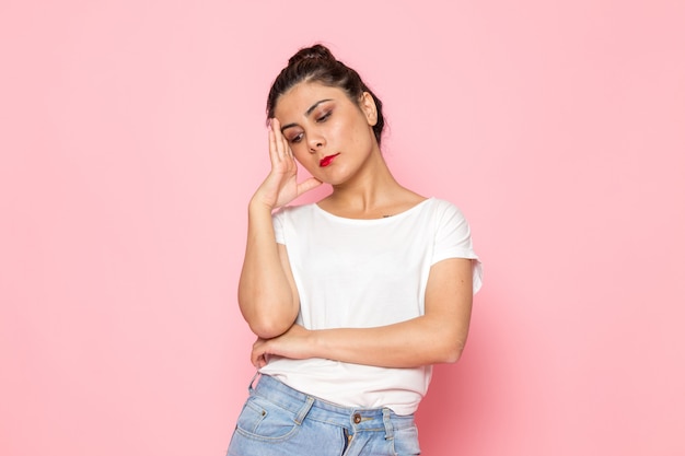 A front view young female in white t-shirt and blue jeans posing with thinking expression