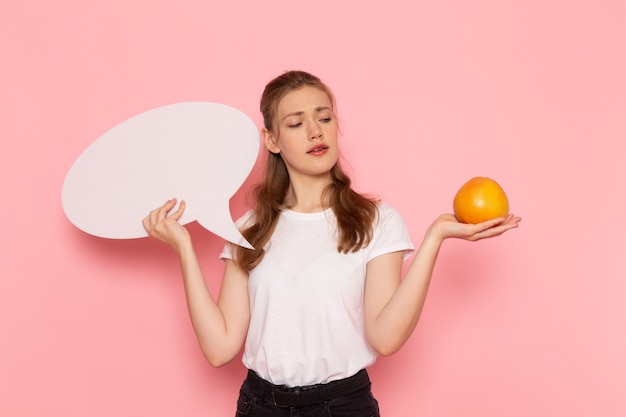 Free photo front view of young female in white t-shirt holding grapefruit and white sign on pink wall