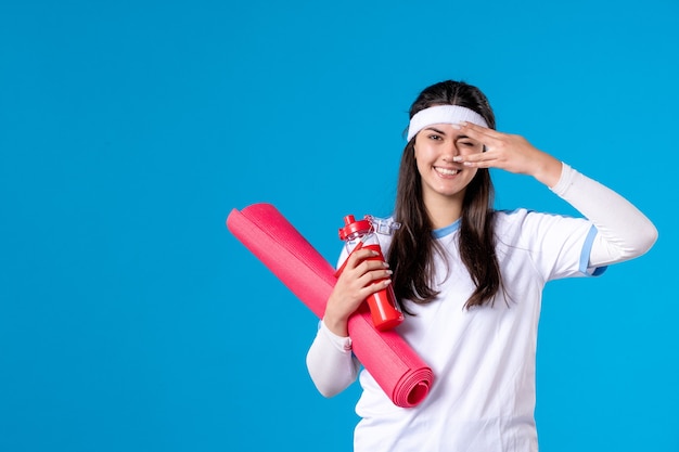 Front view young female with carpet for exercises and bottle of water on blue wall