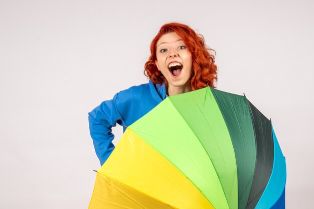 Front view of young female with colorful umbrella on a white wall